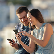 Happy couple sharing smart phones content in a town outskirts on vacation